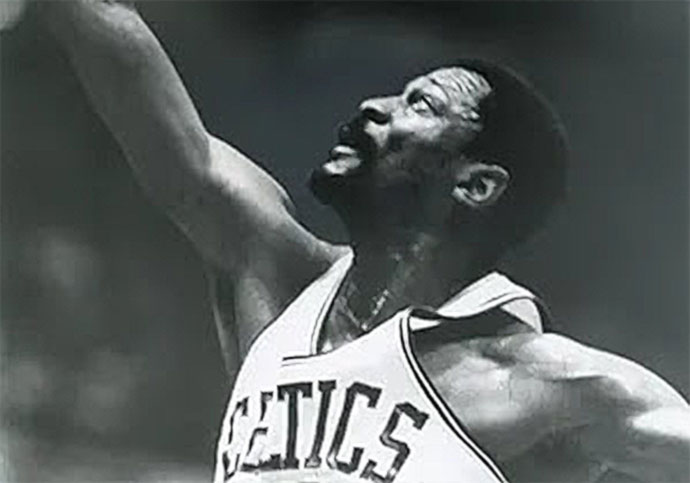 Old Black and white photo of Bill Russell reaching to take a shot in his Celtics jersey