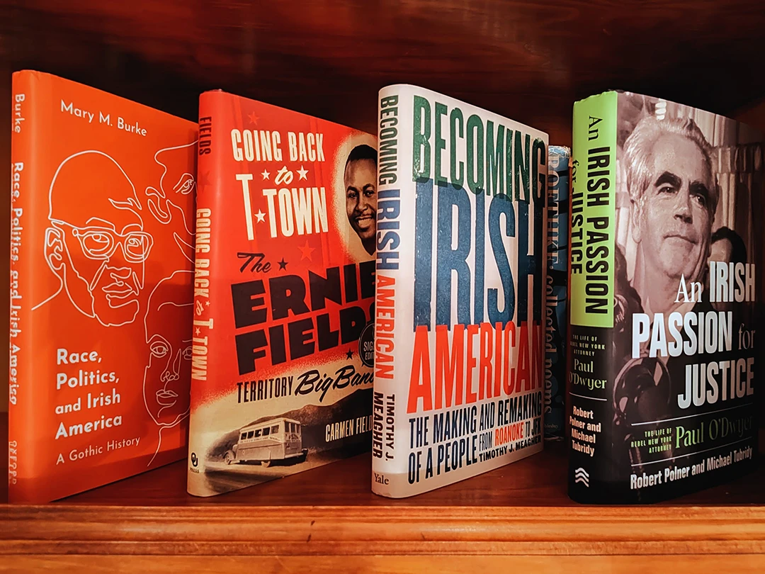 A bookshelf with these books: "Race, Politics, and Irish America: A Gothic History" by Mary M. Burke, "Going Back to T-Town: The Ernie Fields Territory Big Band" by Carmen Fields, "Becoming Irish-American: The Making and Remaking of a People from Roanoke to JFK" by Timothy J. Meagher, and "An Irish Passion for Justice: The Life of Rebel New York Attorney Paul O'Dwyer" by Robert Polner and Michael Tubridy