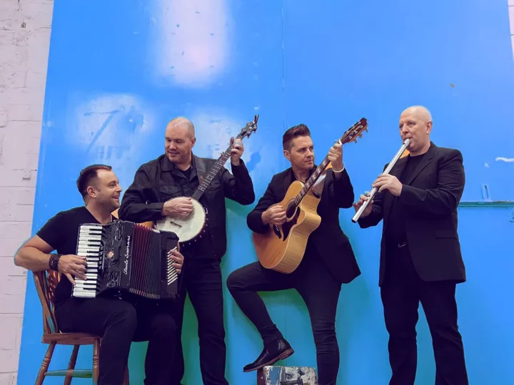 4 members of the High Kings holding there instruments in front of a blue backdrop