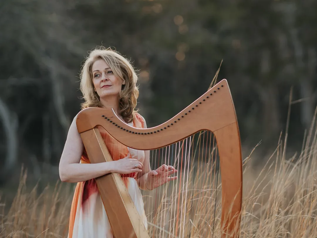 Aine strumming her harm in a field of golden grass and light