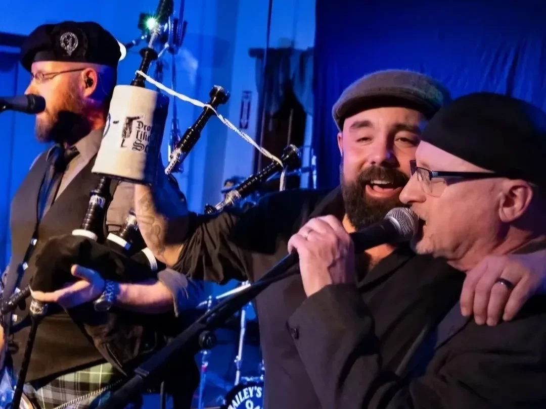 Bailey's Mistake band mates singing into microphone while one raises tankard