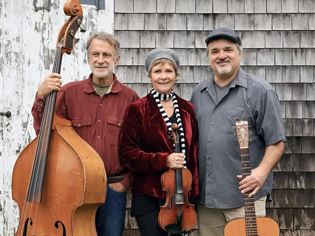 Rose Clancy Trio posed with instruments in front of a weathered building