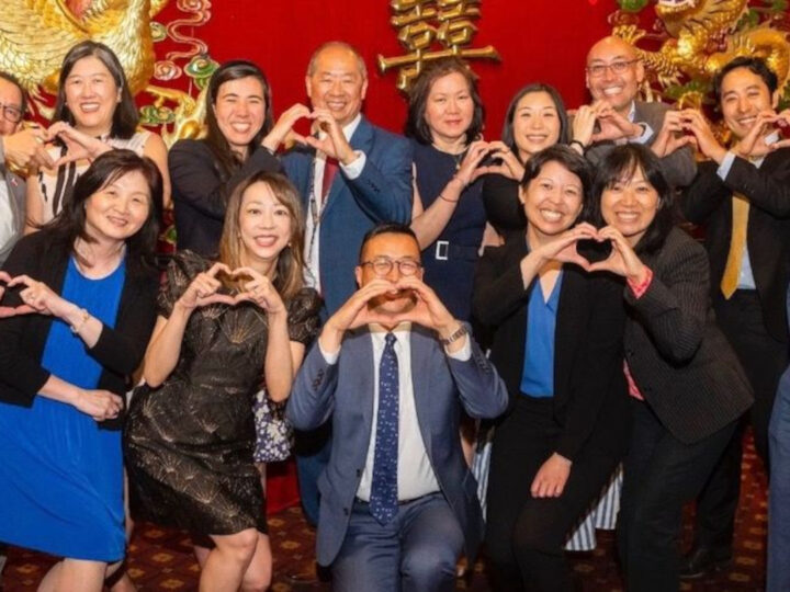 Group of family, friends and colleagues at an Asian Banquet all posing with heart hands